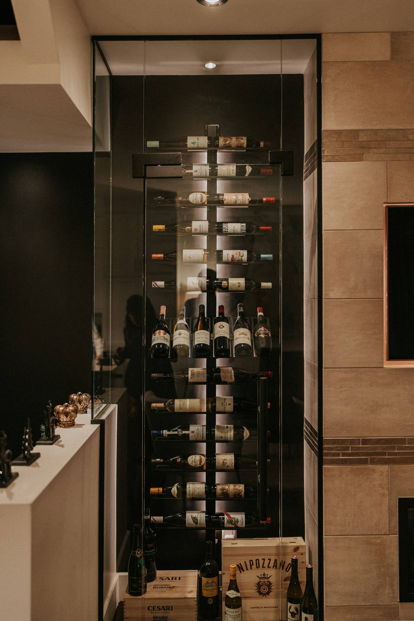 Tall glass-enclosed wine display with black metal framing and bottles on floating pegs