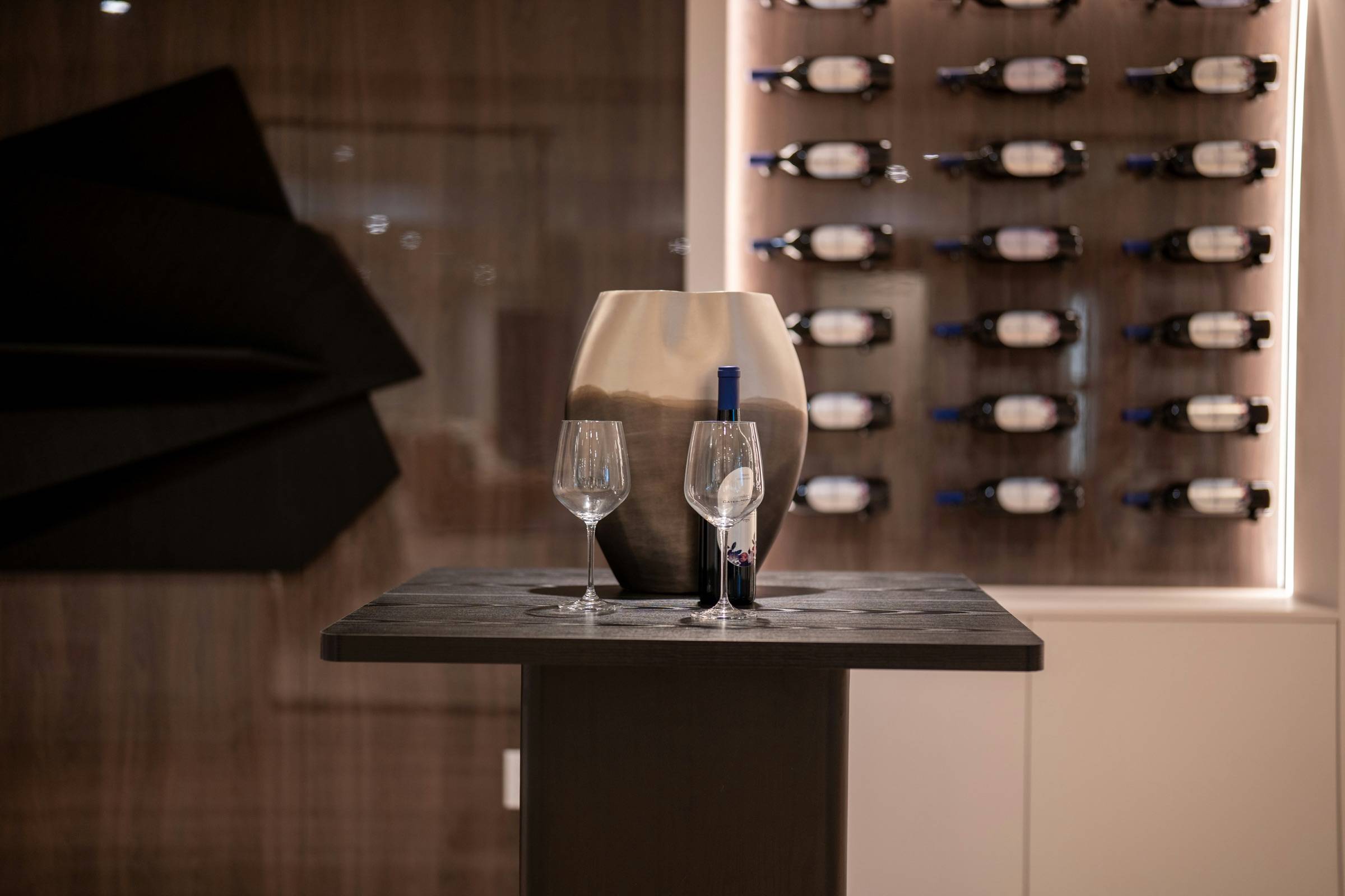 Backlit metal peg wine wall behind a small tasting table with two glasses and a decanter